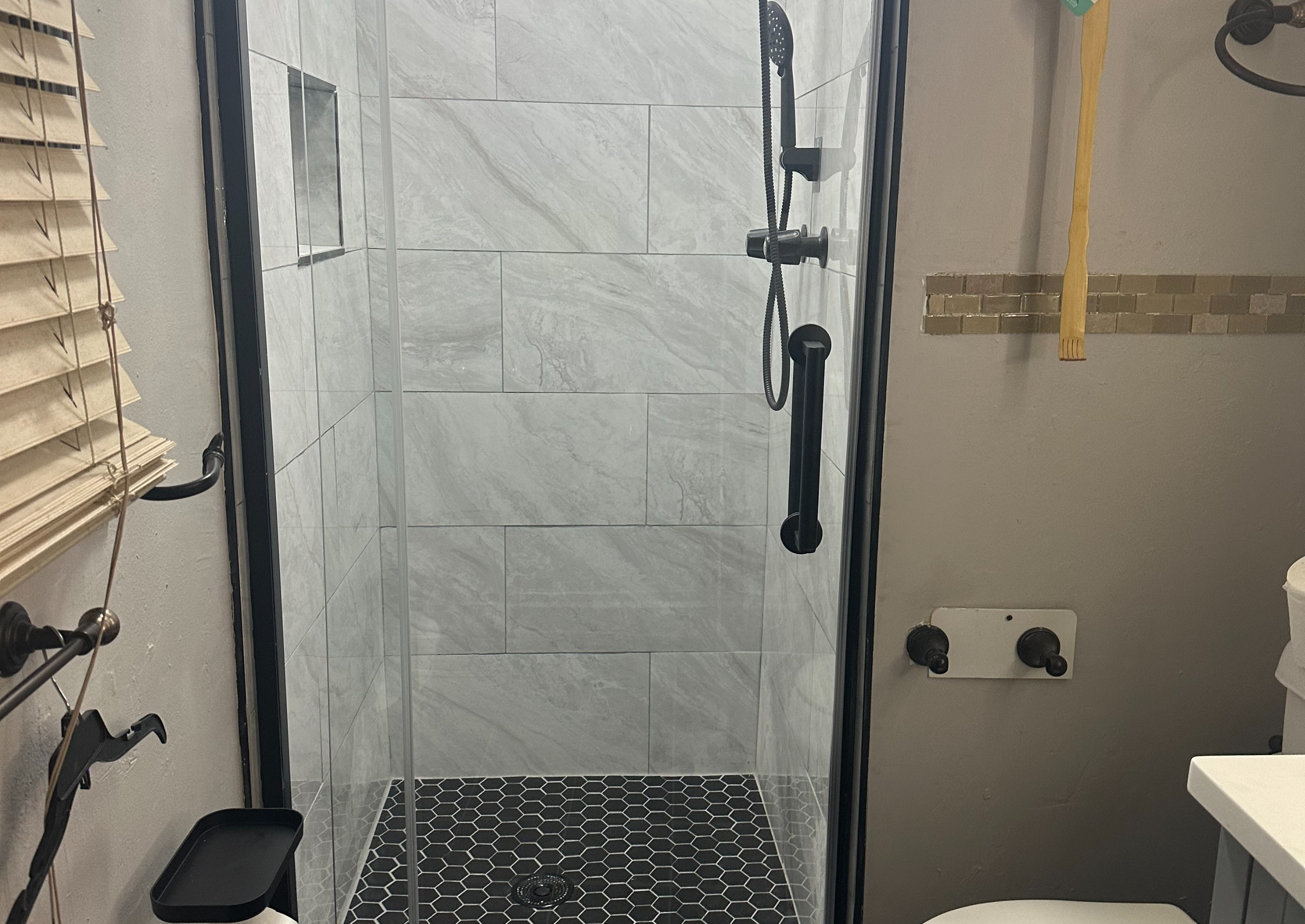 Modern Bathroom Remodel with Black, Hexagon Floor Tiles, Large Marble Wall Tiles, Glass Door, and Sleek Black Shower Head